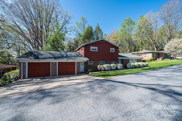 exterior space with a garage, aphalt driveway, brick siding, and a front yard