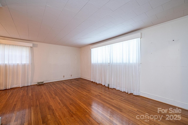 empty room featuring visible vents, baseboards, and hardwood / wood-style flooring