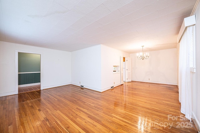 spare room with baseboards, a notable chandelier, and light wood-style floors