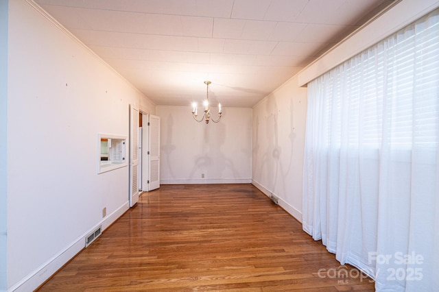 unfurnished dining area with crown molding, visible vents, a chandelier, wood finished floors, and baseboards