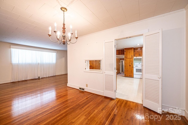 unfurnished room featuring crown molding, baseboards, hardwood / wood-style floors, and an inviting chandelier