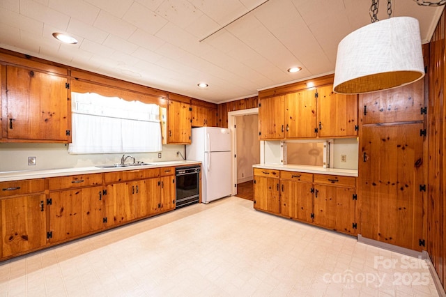 kitchen with a sink, light countertops, freestanding refrigerator, and brown cabinets