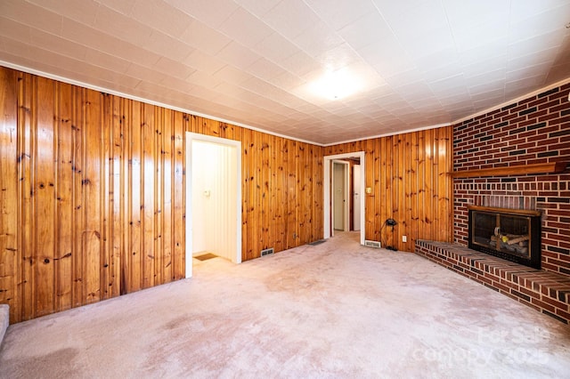 unfurnished living room with visible vents, a fireplace, wooden walls, and carpet