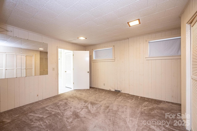 below grade area featuring carpet, visible vents, and wooden walls