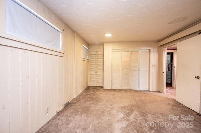 unfurnished bedroom featuring wood walls, two closets, and carpet floors