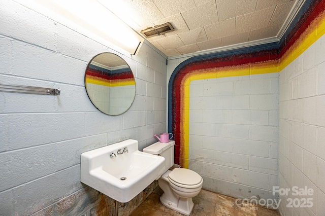 half bathroom featuring toilet, visible vents, a sink, and concrete block wall