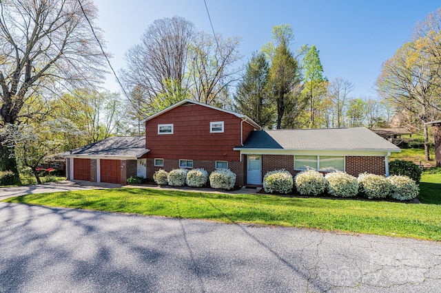 split level home with aphalt driveway, a front yard, brick siding, and an attached garage