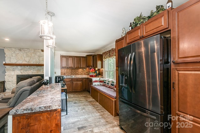 kitchen featuring light wood-style flooring, open floor plan, black refrigerator with ice dispenser, brown cabinetry, and a stone fireplace