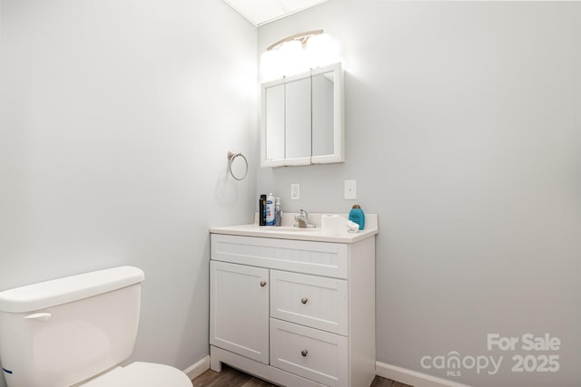 half bath featuring baseboards, wood finished floors, vanity, and toilet