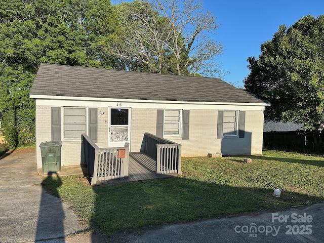 view of front of property with brick siding, a front lawn, and roof with shingles