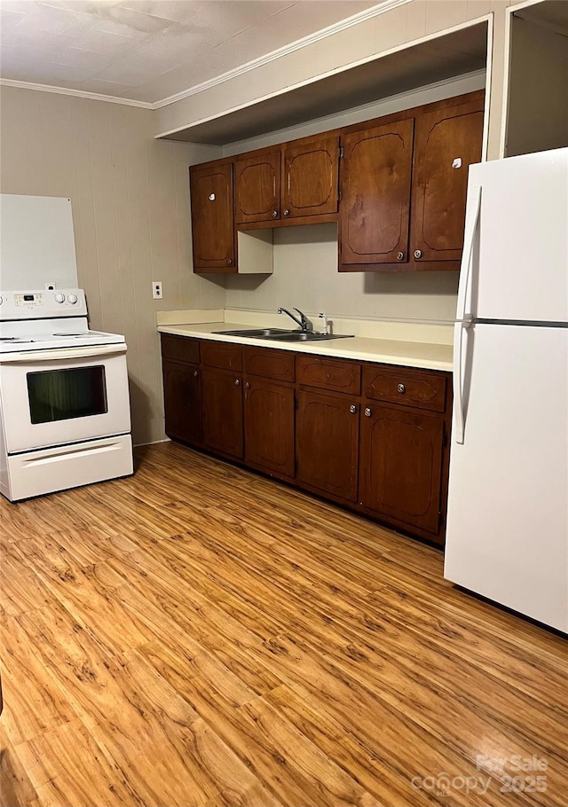 kitchen featuring white appliances, light countertops, crown molding, light wood finished floors, and a sink