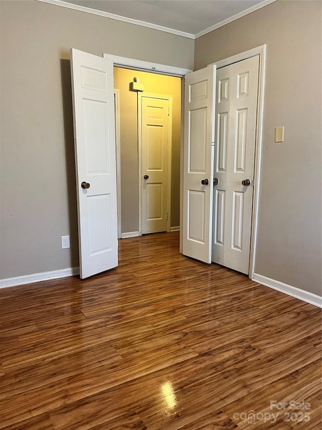 unfurnished bedroom featuring a closet, baseboards, ornamental molding, and wood finished floors