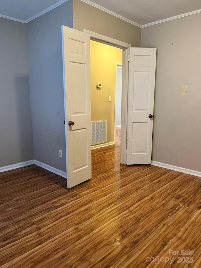 unfurnished room with visible vents, baseboards, crown molding, and wood finished floors