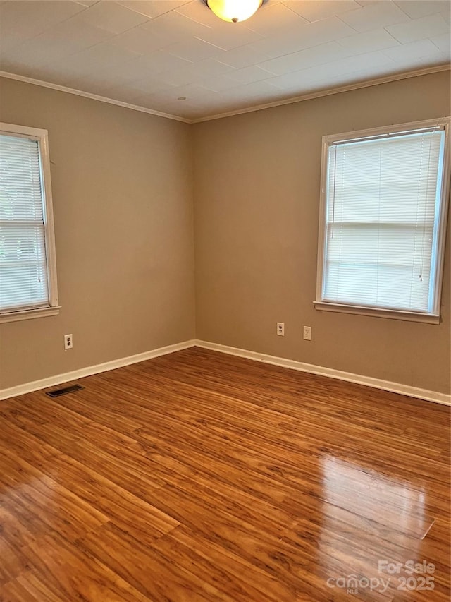 unfurnished room featuring crown molding, wood finished floors, baseboards, and visible vents