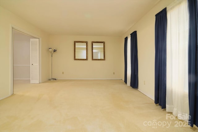 spare room featuring light carpet and baseboards