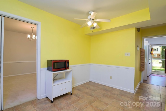 spare room featuring ceiling fan with notable chandelier, wainscoting, and visible vents