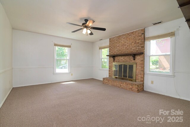 unfurnished living room featuring a fireplace, a ceiling fan, visible vents, carpet flooring, and wainscoting