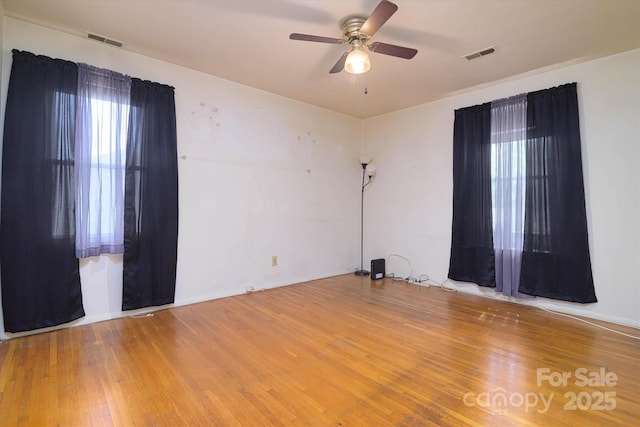 unfurnished room with wood finished floors, ceiling fan, baseboards, and visible vents