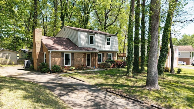 traditional-style house featuring a chimney, aphalt driveway, a front lawn, and brick siding
