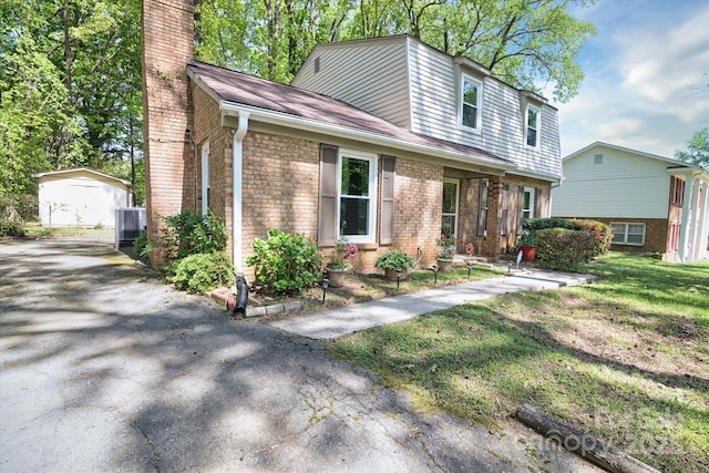 view of front facade featuring a front yard, an outbuilding, aphalt driveway, a chimney, and brick siding