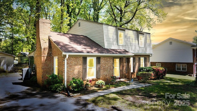 view of front of home featuring a yard, brick siding, central air condition unit, and a chimney