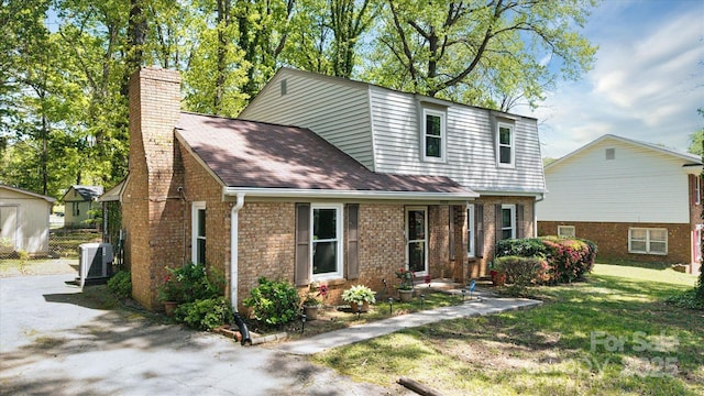 view of front of home with cooling unit, a chimney, a front yard, and brick siding