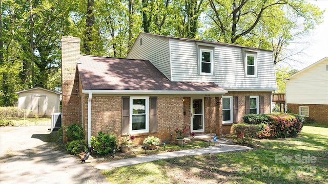 view of front of home featuring a front yard, brick siding, central air condition unit, and a chimney