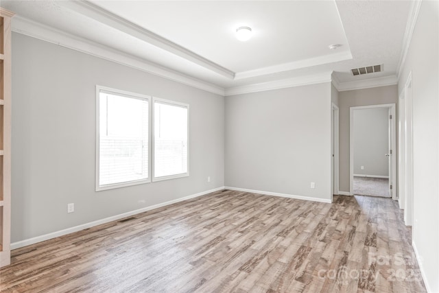 spare room with visible vents, crown molding, a tray ceiling, baseboards, and light wood-style floors