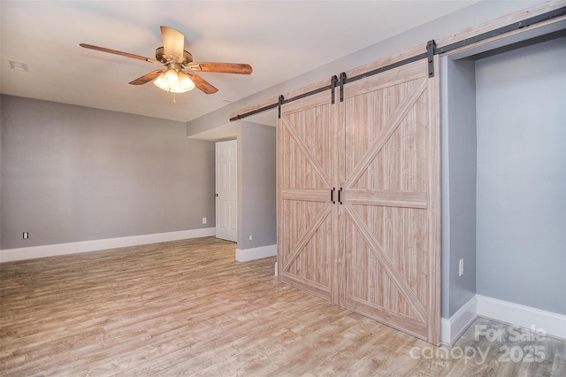 6008 Corkstone Dr, Mint Hill, NC 28227 - unfurnished bedroom with a barn door, light wood-style floors, baseboards, and a ceiling fan
