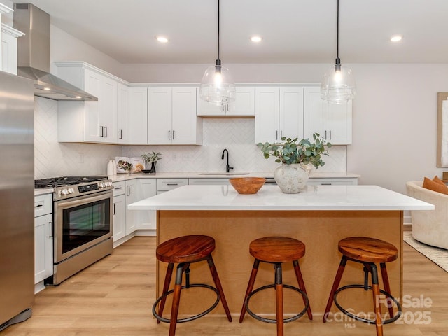 kitchen featuring appliances with stainless steel finishes, wall chimney exhaust hood, a sink, light wood-style flooring, and a kitchen island