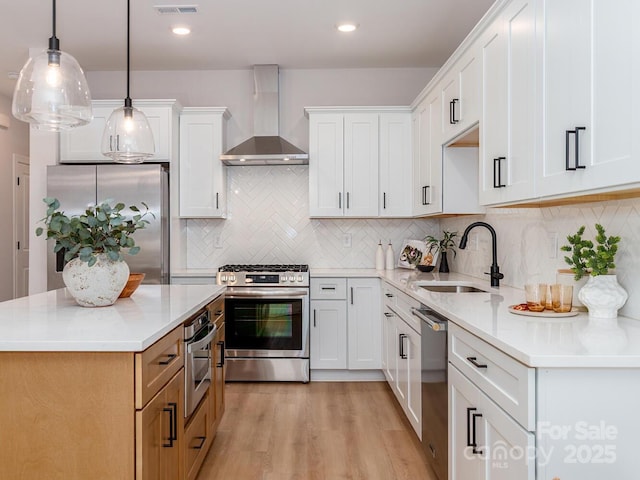 kitchen with wall chimney exhaust hood, stainless steel appliances, a sink, light wood-type flooring, and light countertops