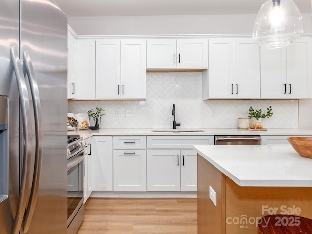 kitchen with appliances with stainless steel finishes, a sink, decorative backsplash, and white cabinets