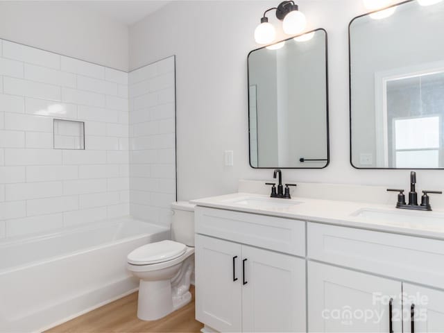 bathroom with toilet, wood finished floors, double vanity, and washtub / shower combination