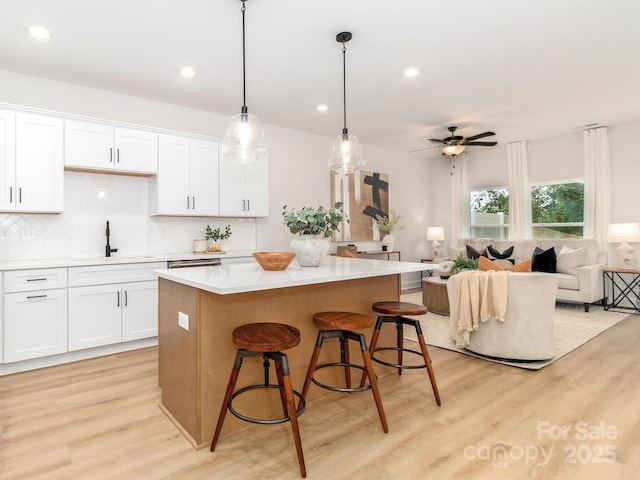 kitchen with a sink, light wood-type flooring, a center island, tasteful backsplash, and white cabinetry