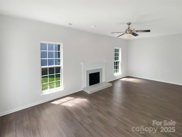 unfurnished living room with a fireplace, ceiling fan, baseboards, and dark wood finished floors