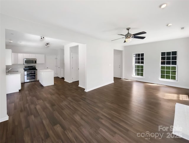 unfurnished living room with a sink, baseboards, ceiling fan, and dark wood finished floors