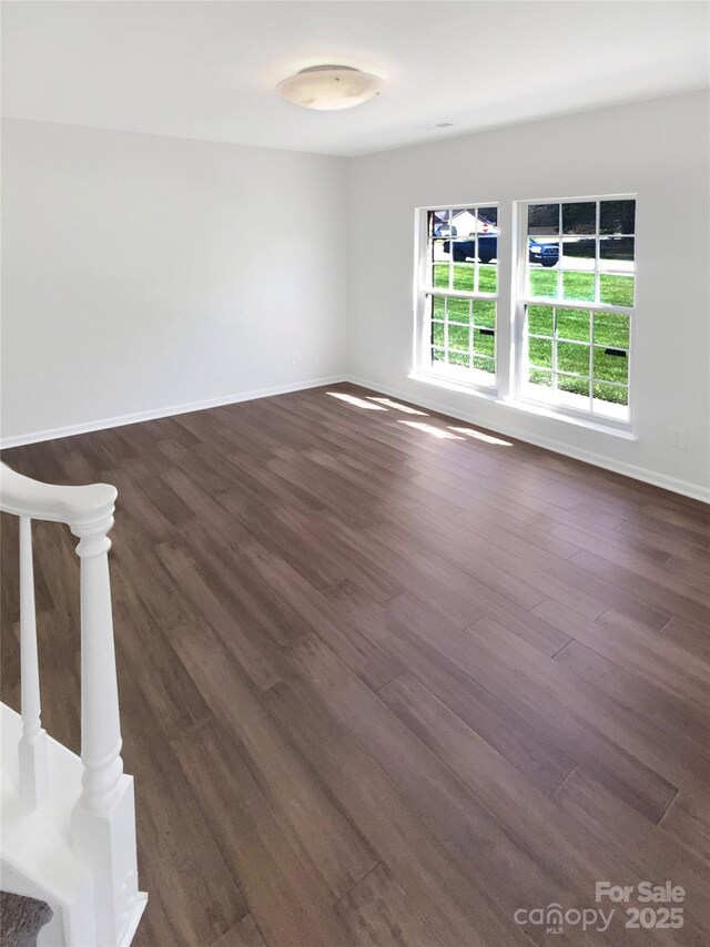empty room featuring baseboards and dark wood finished floors