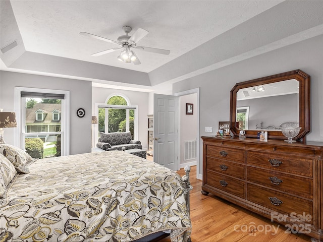 bedroom with light wood finished floors, visible vents, ceiling fan, and a raised ceiling