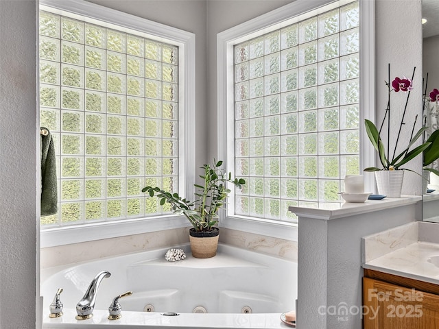 full bath with vanity, a whirlpool tub, and a textured wall