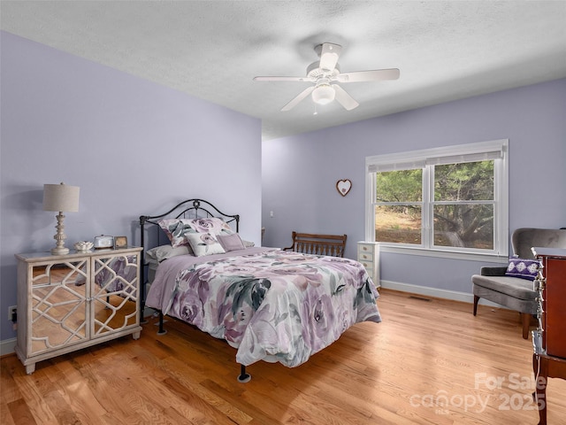 bedroom with a textured ceiling, ceiling fan, visible vents, baseboards, and wood finished floors