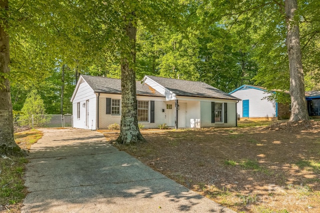 view of front of home featuring fence, driveway, brick siding, and an outdoor structure