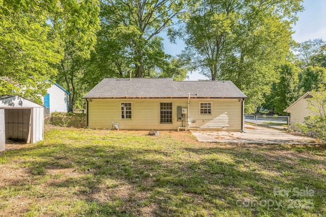 back of house featuring fence, a storage shed, an outdoor structure, a patio, and a lawn