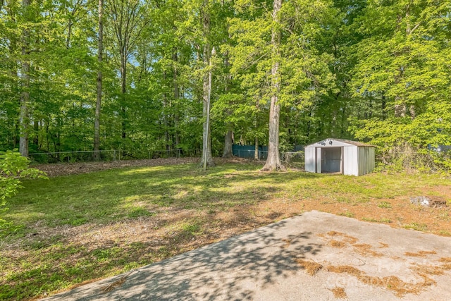 view of yard featuring a wooded view, a storage shed, an outdoor structure, fence, and a patio
