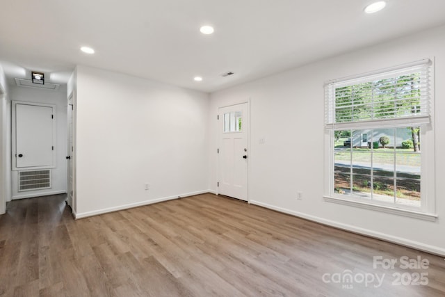 empty room with a wealth of natural light, wood finished floors, visible vents, and recessed lighting