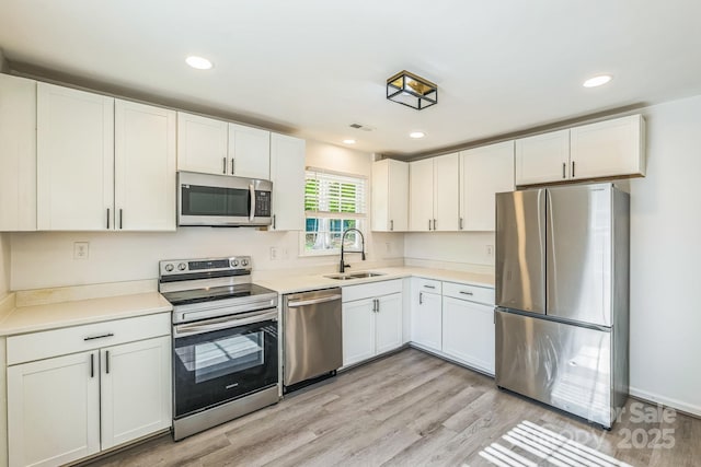 kitchen with white cabinets, stainless steel appliances, visible vents, a sink, and light wood-type flooring