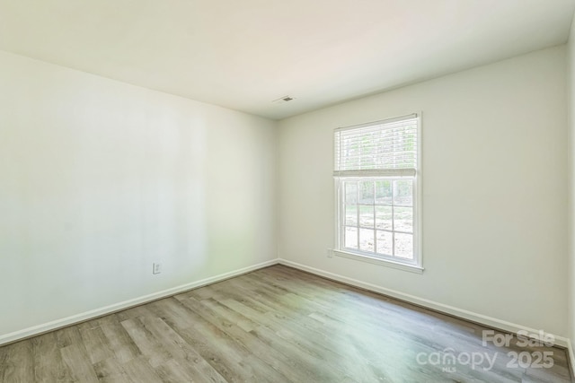 empty room featuring baseboards, wood finished floors, and visible vents