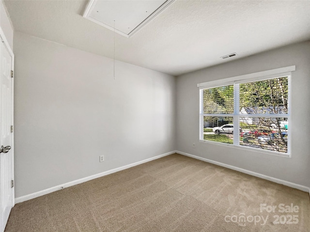 unfurnished room with carpet flooring, baseboards, attic access, and visible vents
