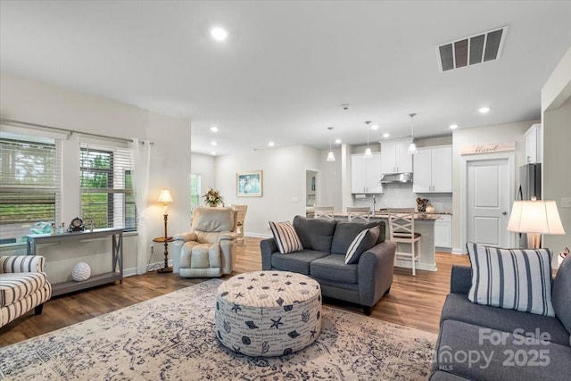 living area with recessed lighting, light wood-type flooring, visible vents, and baseboards