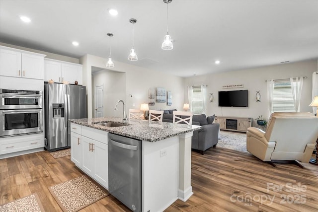 kitchen featuring white cabinets, stainless steel appliances, open floor plan, and a sink
