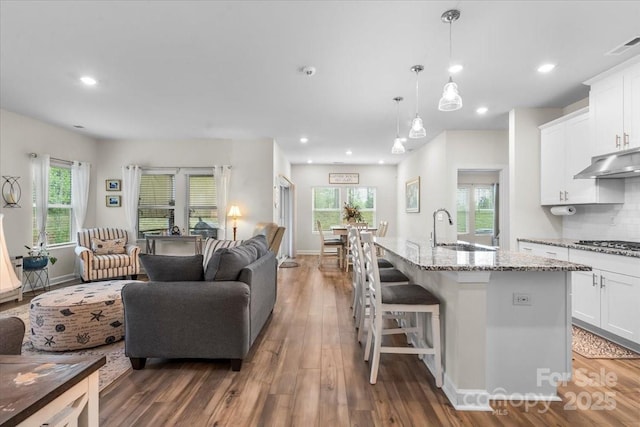 kitchen featuring wood finished floors, a sink, open floor plan, white cabinets, and light stone countertops